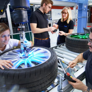 Vier Personen arbeiten zusammen mit Roboter an Autoreifen